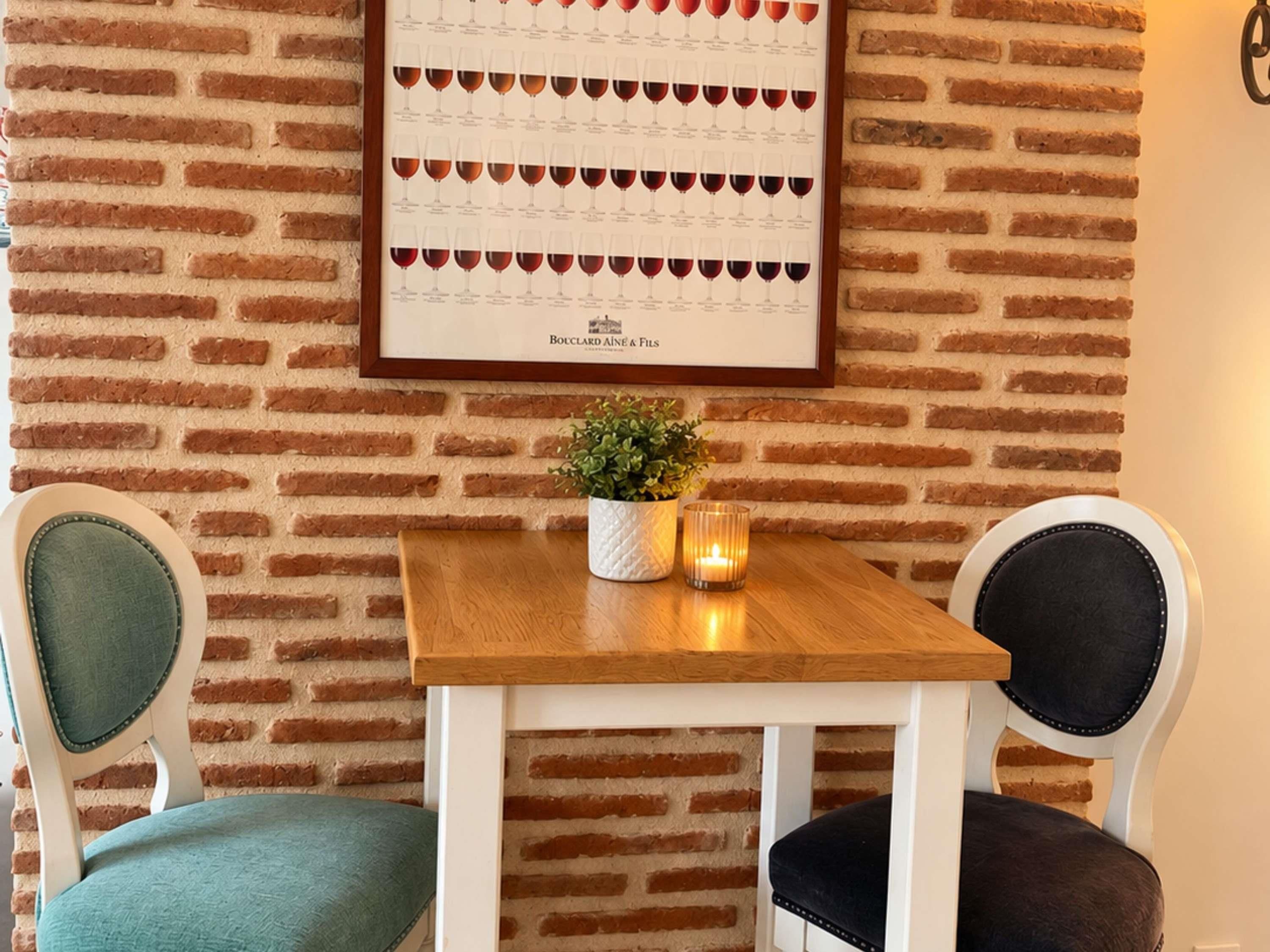 A dining area with a brick wall, a framed menu, a small table with a candle, and two chairs.