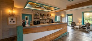 A bar area with a wooden counter, shelves with bottles, and a mural on the ceiling.