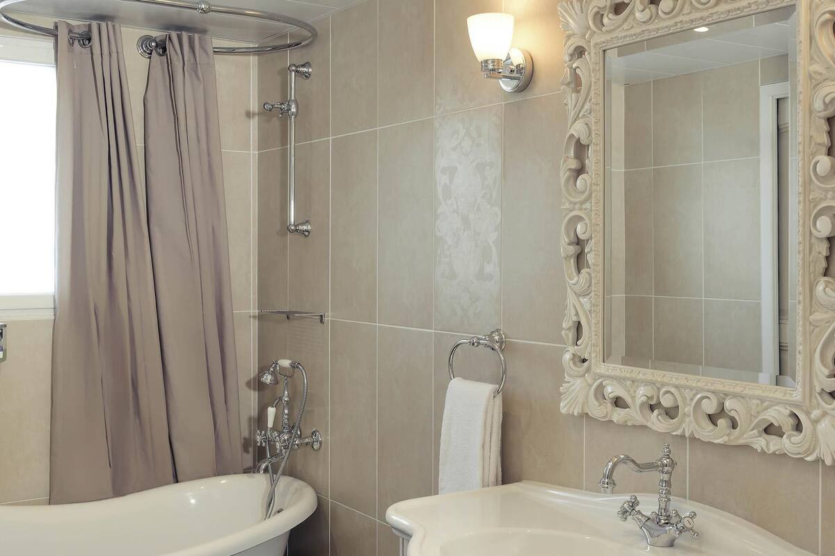 Ein Badezimmer mit einer Badewanne, einem Waschbecken, einer Dusche und einem Spiegel mit aufwendiger Verzierung.