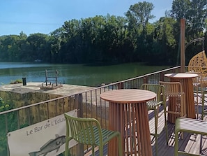 A wooden deck with tables and chairs overlooking a calm body of water, with a sign reading 'Le Bar de L'Eclus.' - Hôtel Mercure Villeneuve sur Lot Moulin de Madame (Villeneuve-sur-Lot)