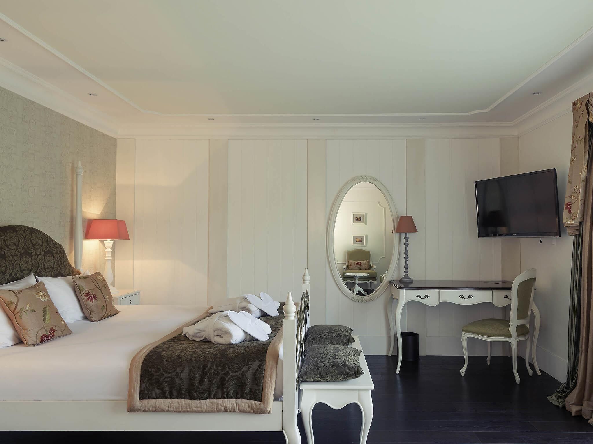 Una habitación de hotel con cama, escritorio, silla, televisor y espejo.