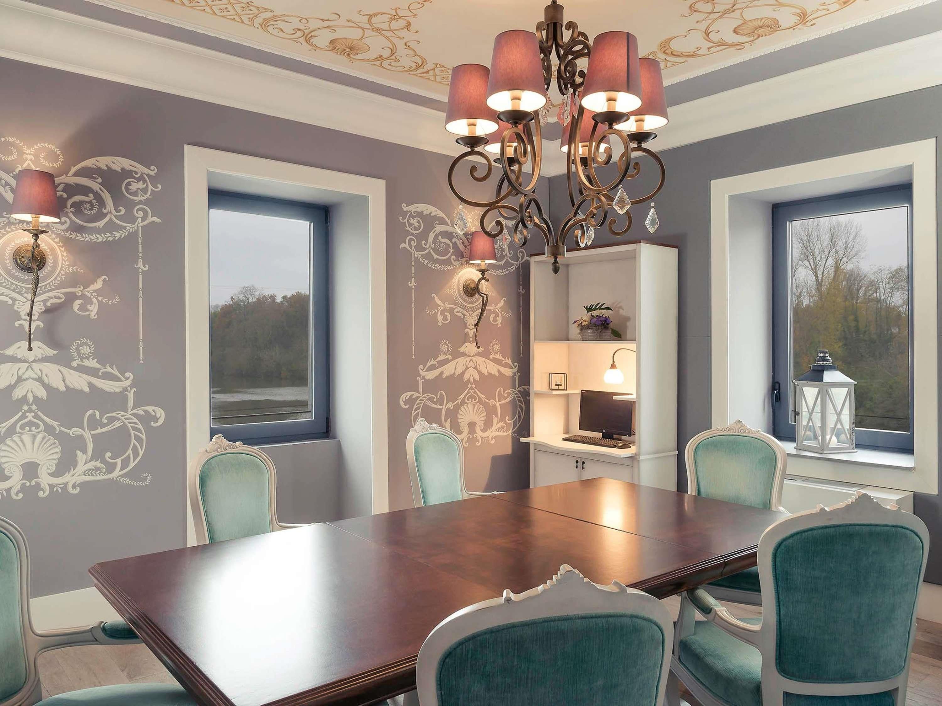 A dining room with a large table, chairs, a chandelier, and decorative wall patterns.