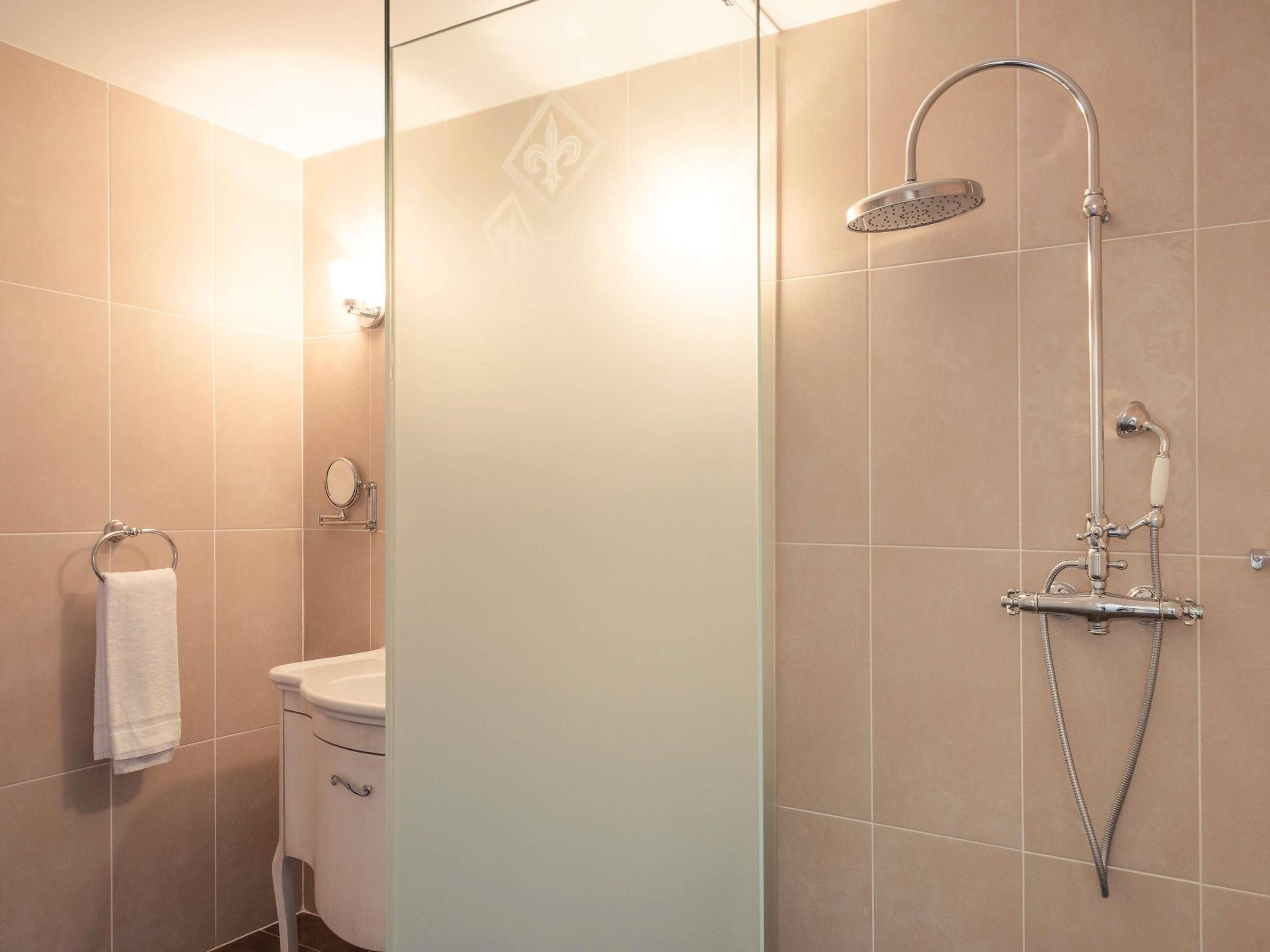 A modern bathroom with a glass partition, a shower with a handheld showerhead, a toilet, and a towel rack.