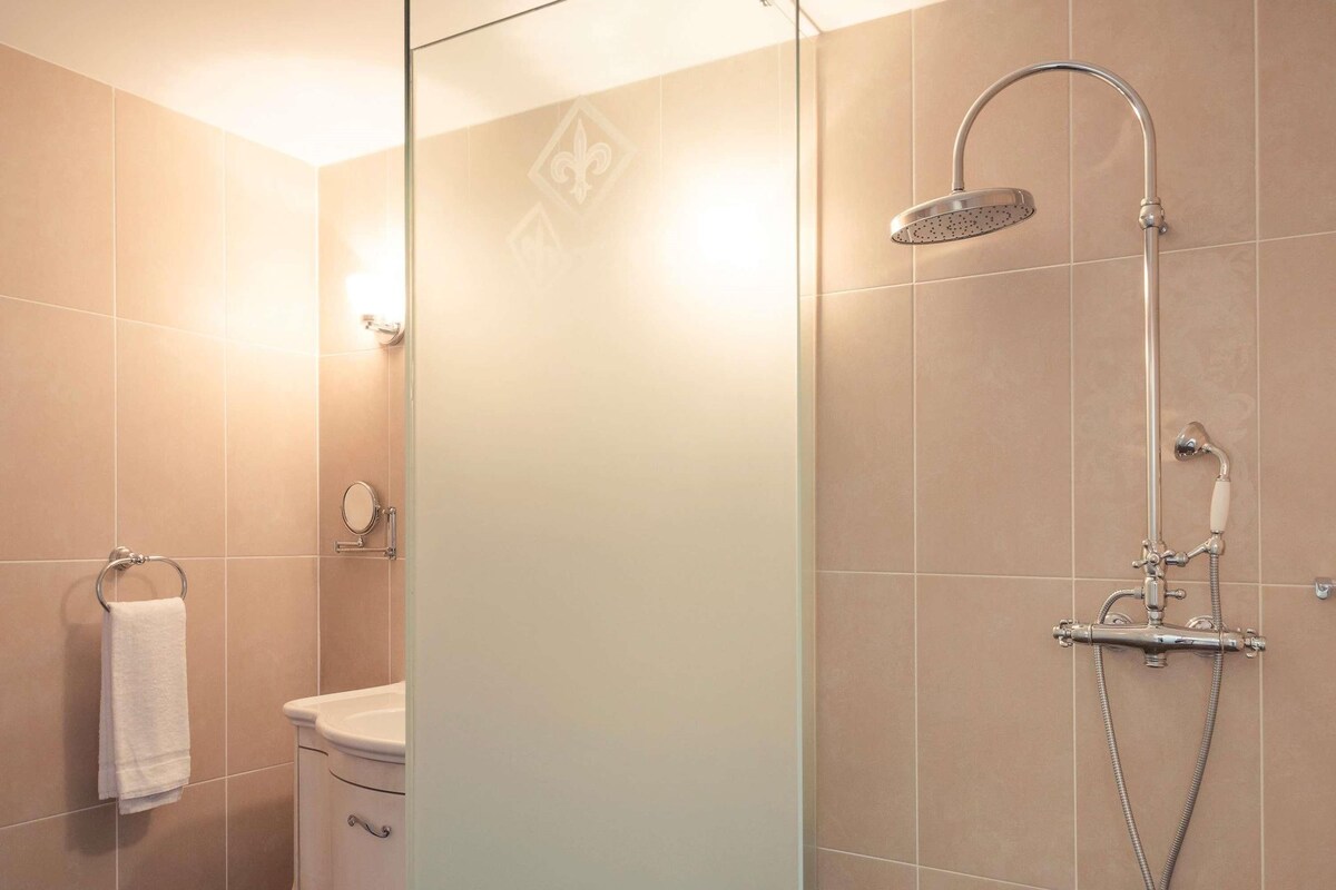 A modern bathroom with a glass partition, a shower with a handheld showerhead, a toilet, and a towel rack.