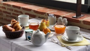A breakfast table with croissants, fruit, tea, and coffee, set against a brick wall with a view of trees and buildings.