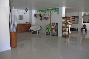A spacious living room with a large potted plant, a wooden bookshelf, and a white chair.