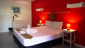 A hotel room with a large bed, two bedside tables with lamps, a white bedside table with a vase, and a mirror on the wall.