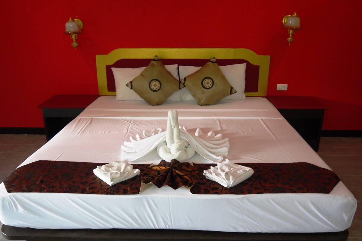 A neatly made bed with a white comforter, two decorative pillows, and a towel arrangement.