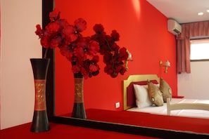 A room with a bed, a mirror, and a vase with red flowers.