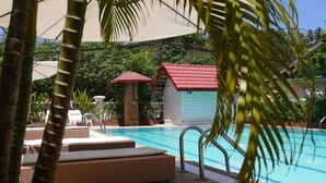 A pool area with lounge chairs, a small building with a red roof, and palm trees.