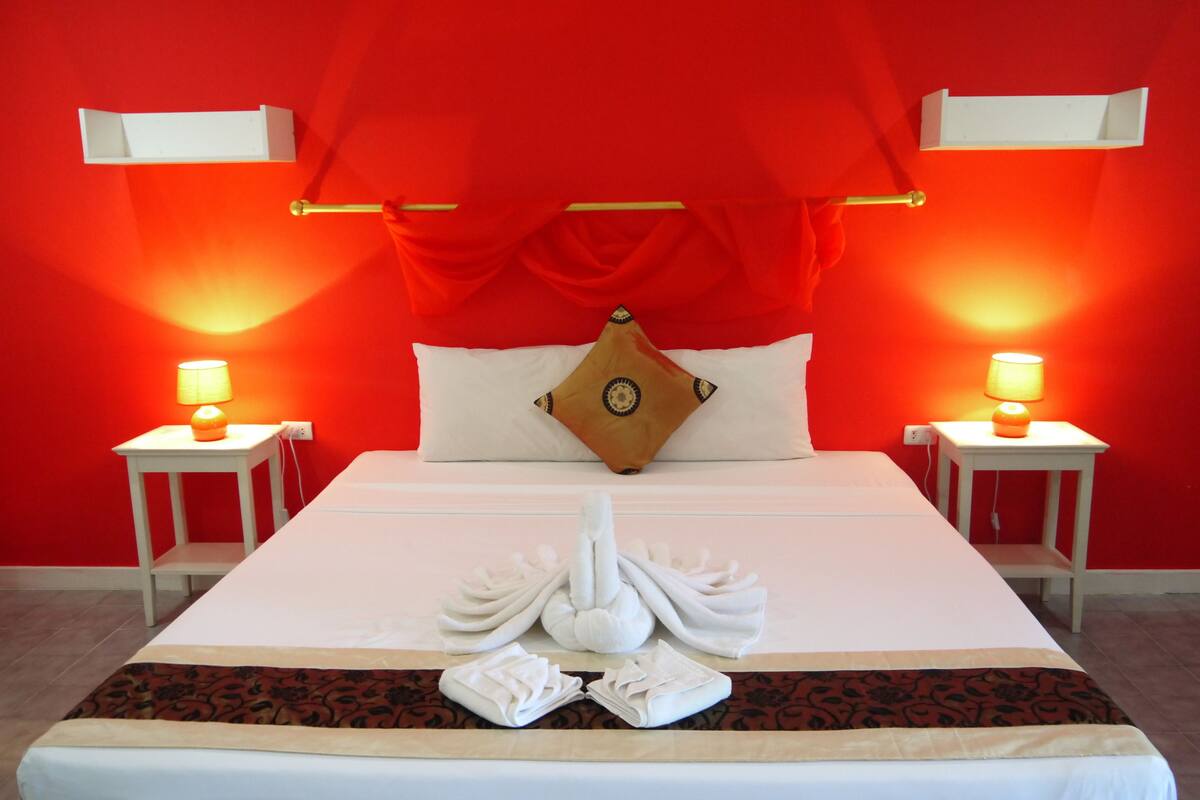 A hotel room with a large bed, two bedside tables with lamps, a red wall, and a decorative pillow.