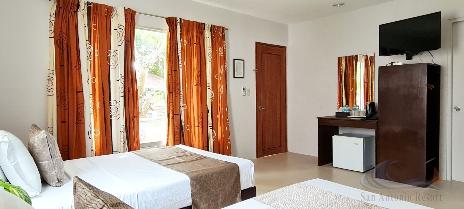 A hotel room with two beds, a desk, a television, and a small refrigerator.