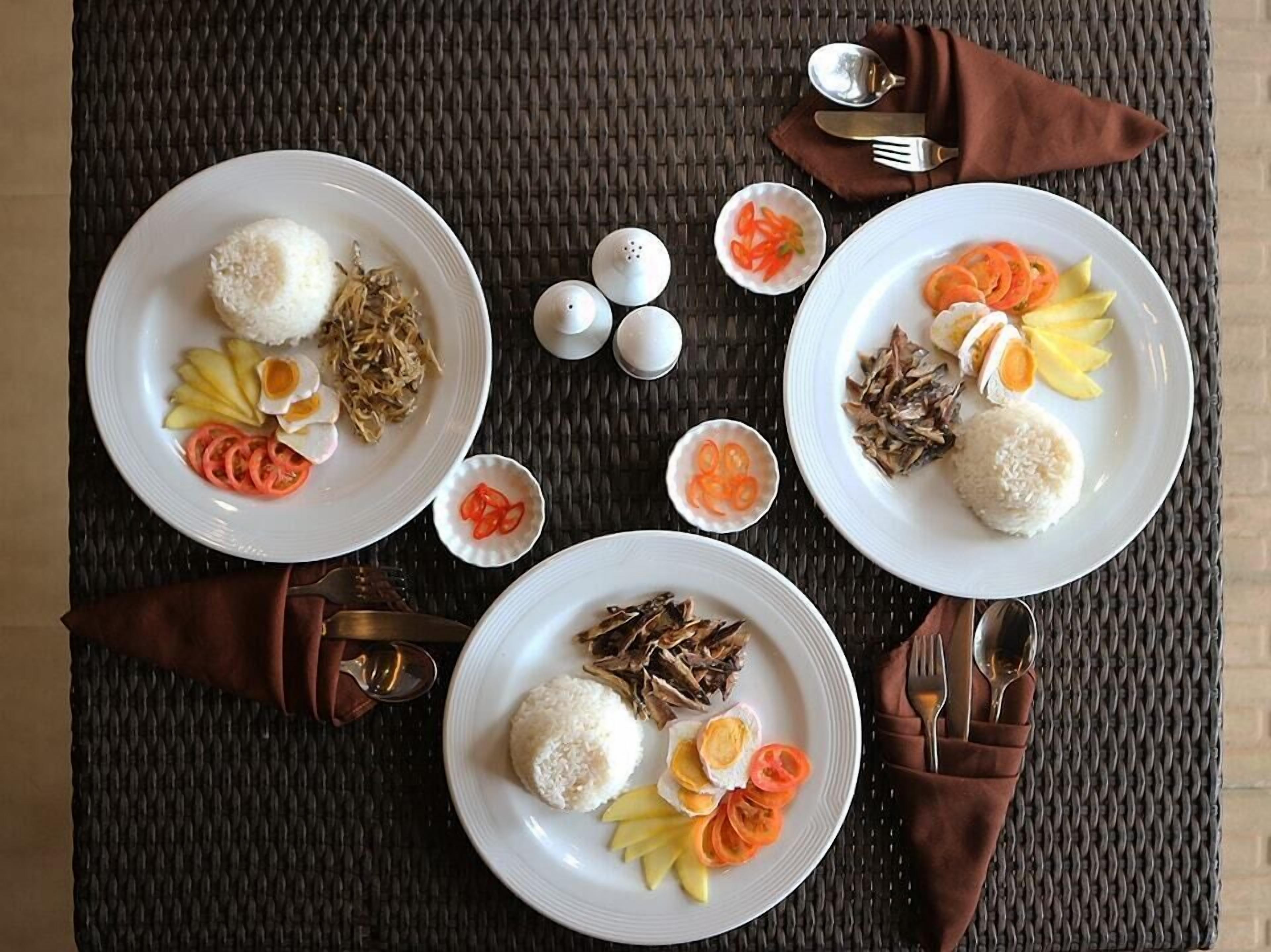 Two white plates with rice, sliced vegetables, and a boiled egg, arranged on a woven table mat.