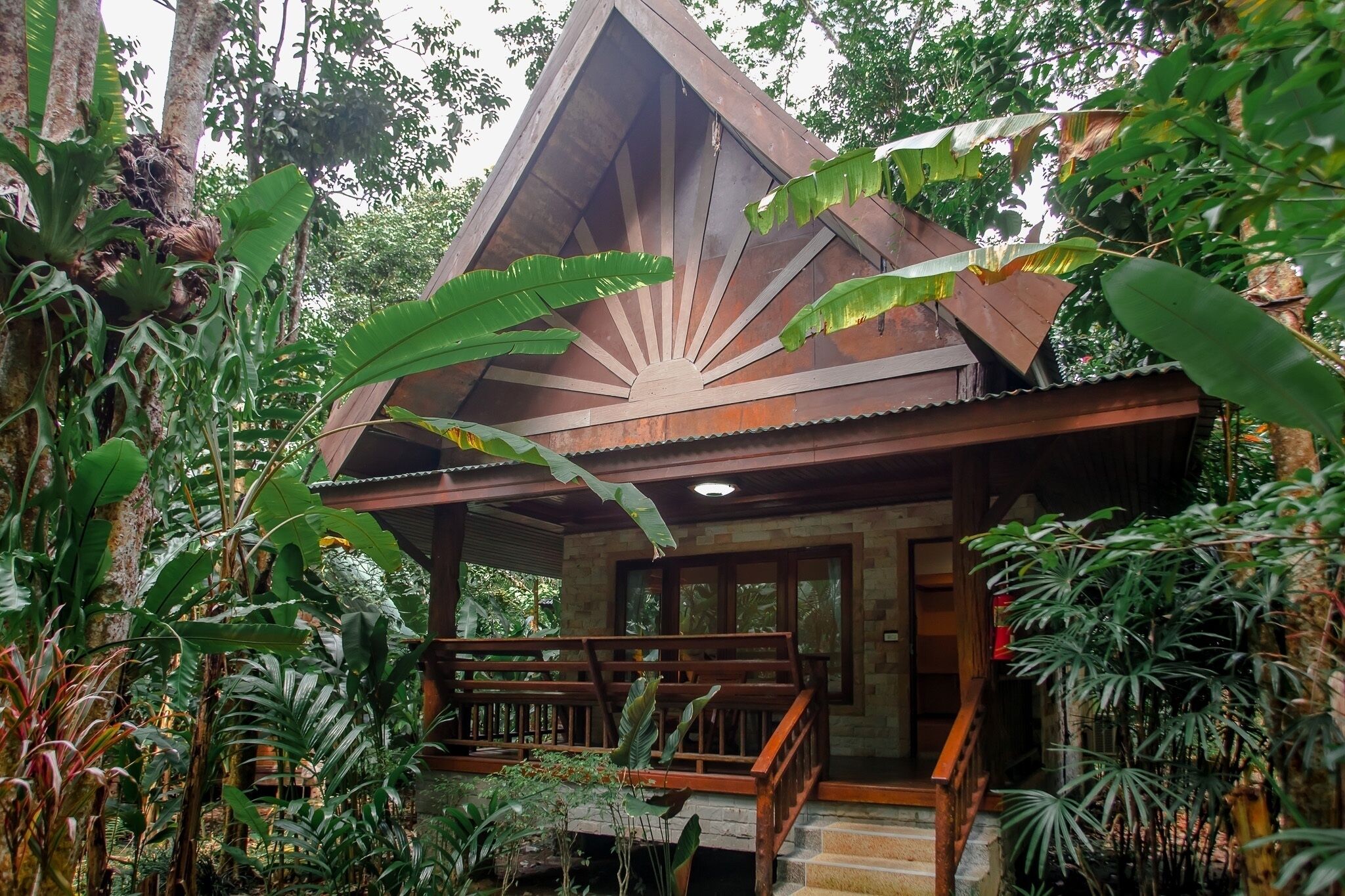 A wooden cabin with a sloped roof surrounded by dense tropical vegetation.