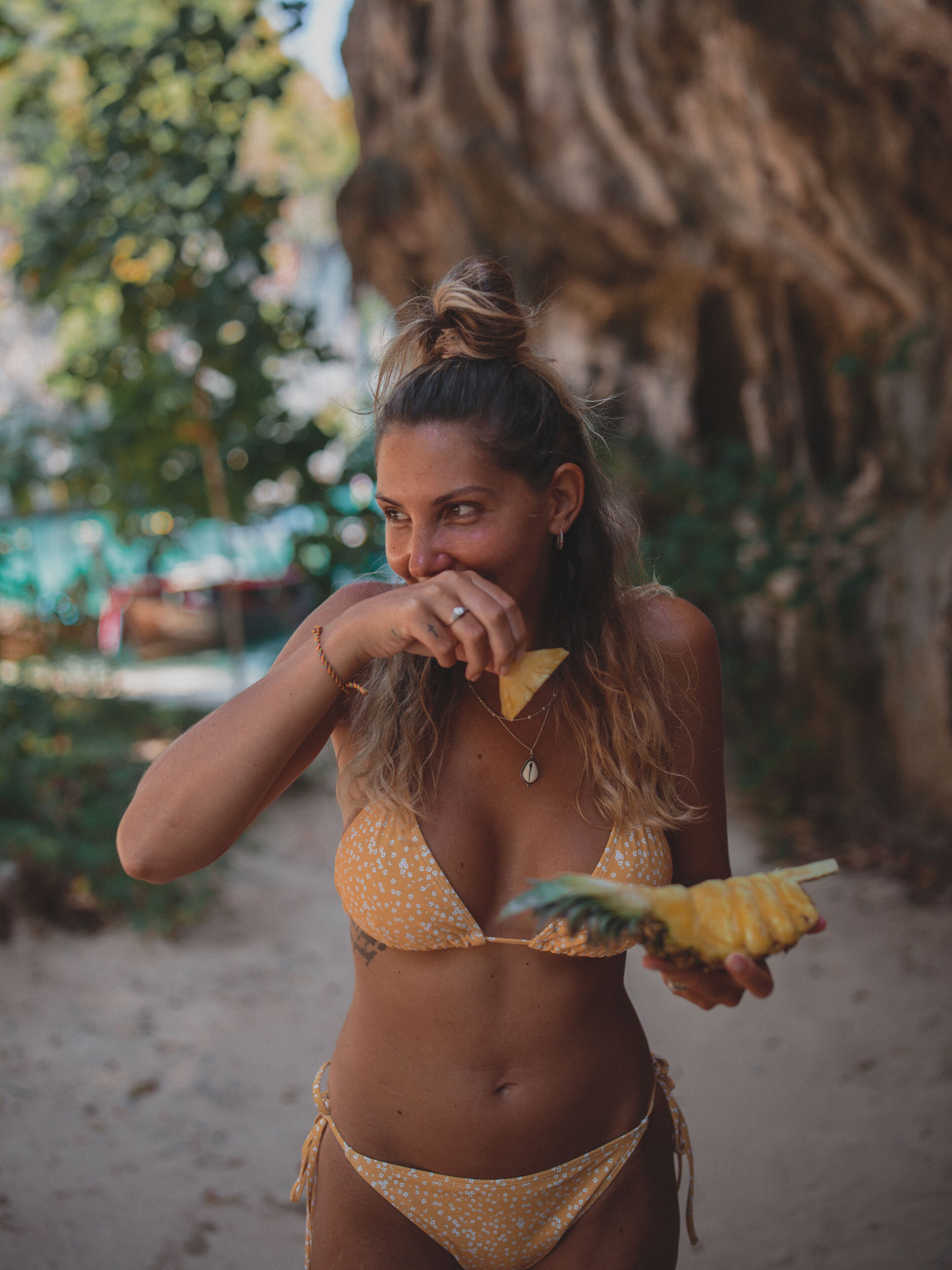 A person in a yellow bikini holding a pineapple.