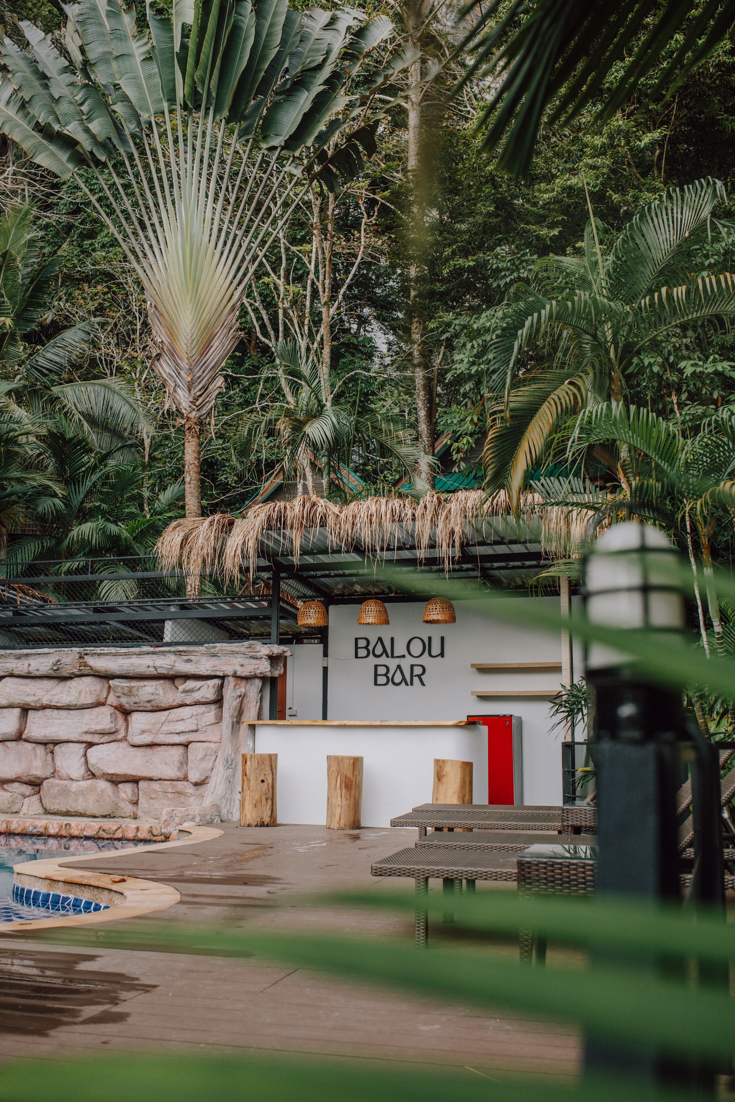 A Balou Bar with a stone wall, wooden benches, and a thatched roof.