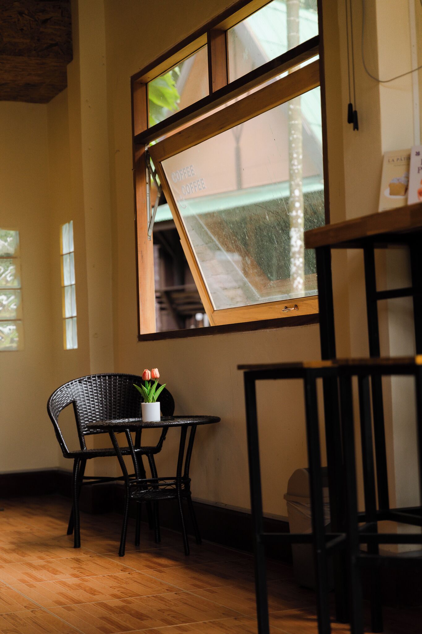 A room with a wooden-framed window, a small table with a potted plant, and two chairs.