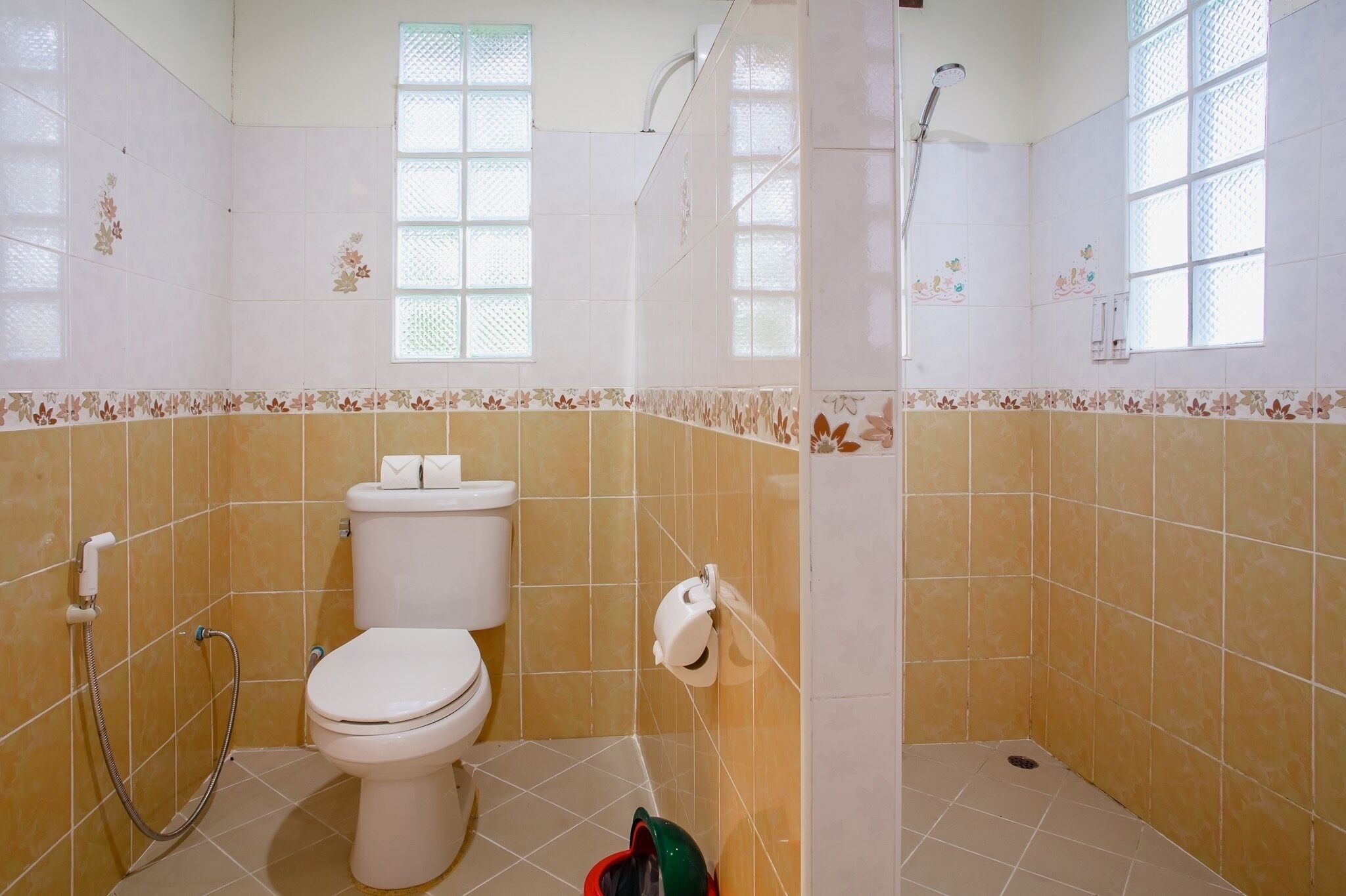 A bathroom with a toilet, shower, and a window.