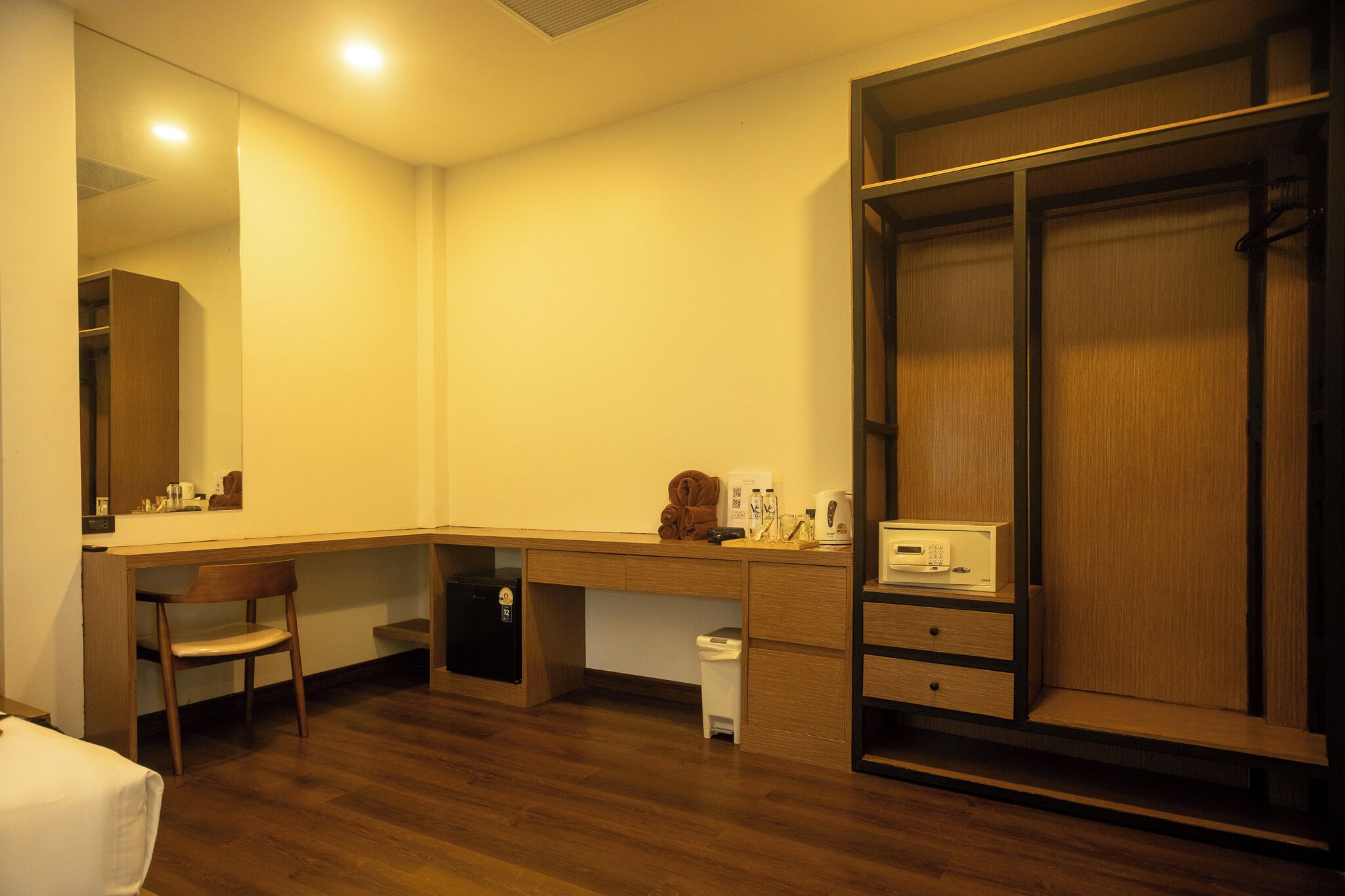 Une chambre d’hôtel avec un bureau en bois, une chaise, une armoire et une petite poubelle.