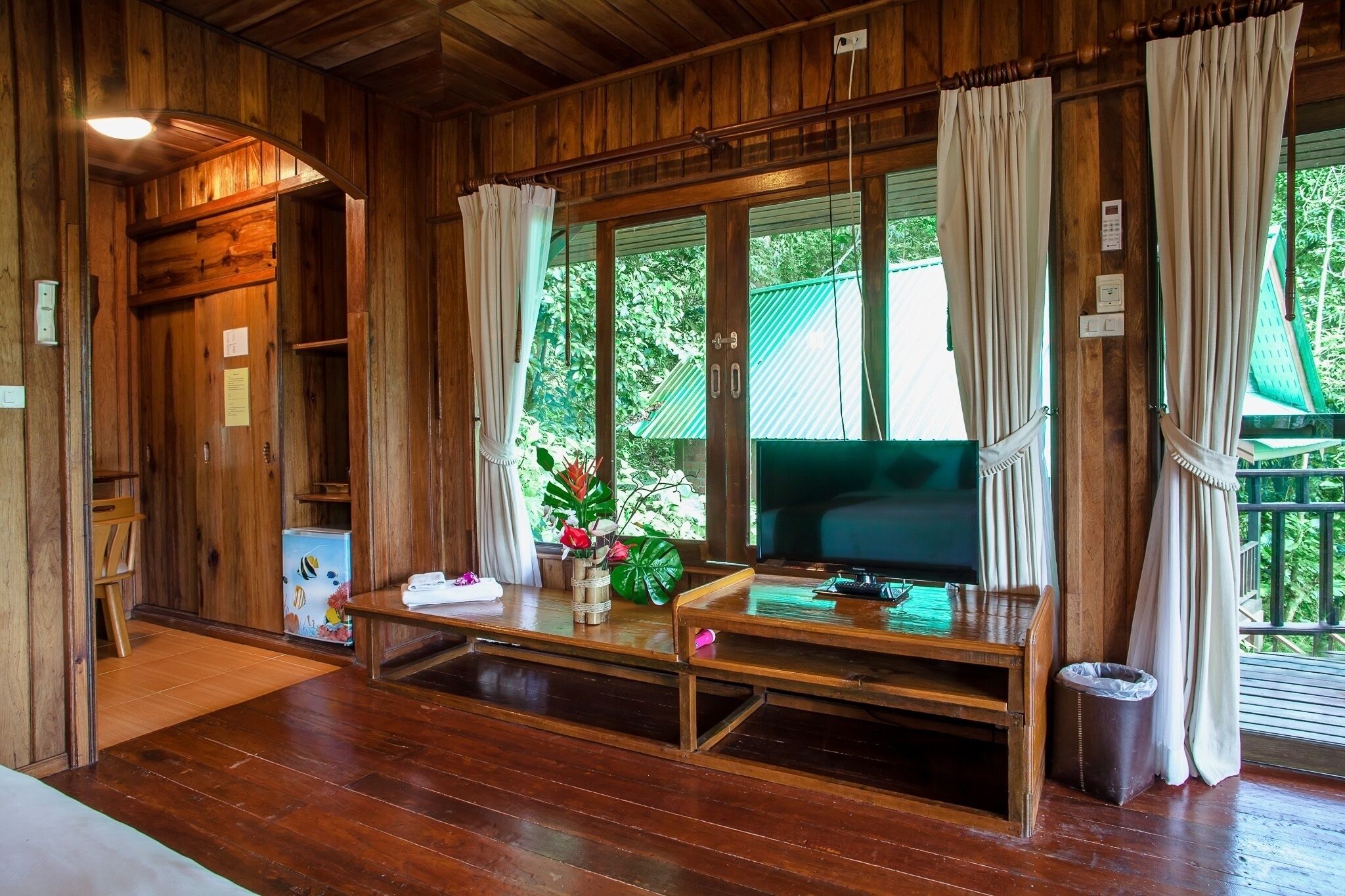 A wooden interior with a television, a small table, and a window with curtains.