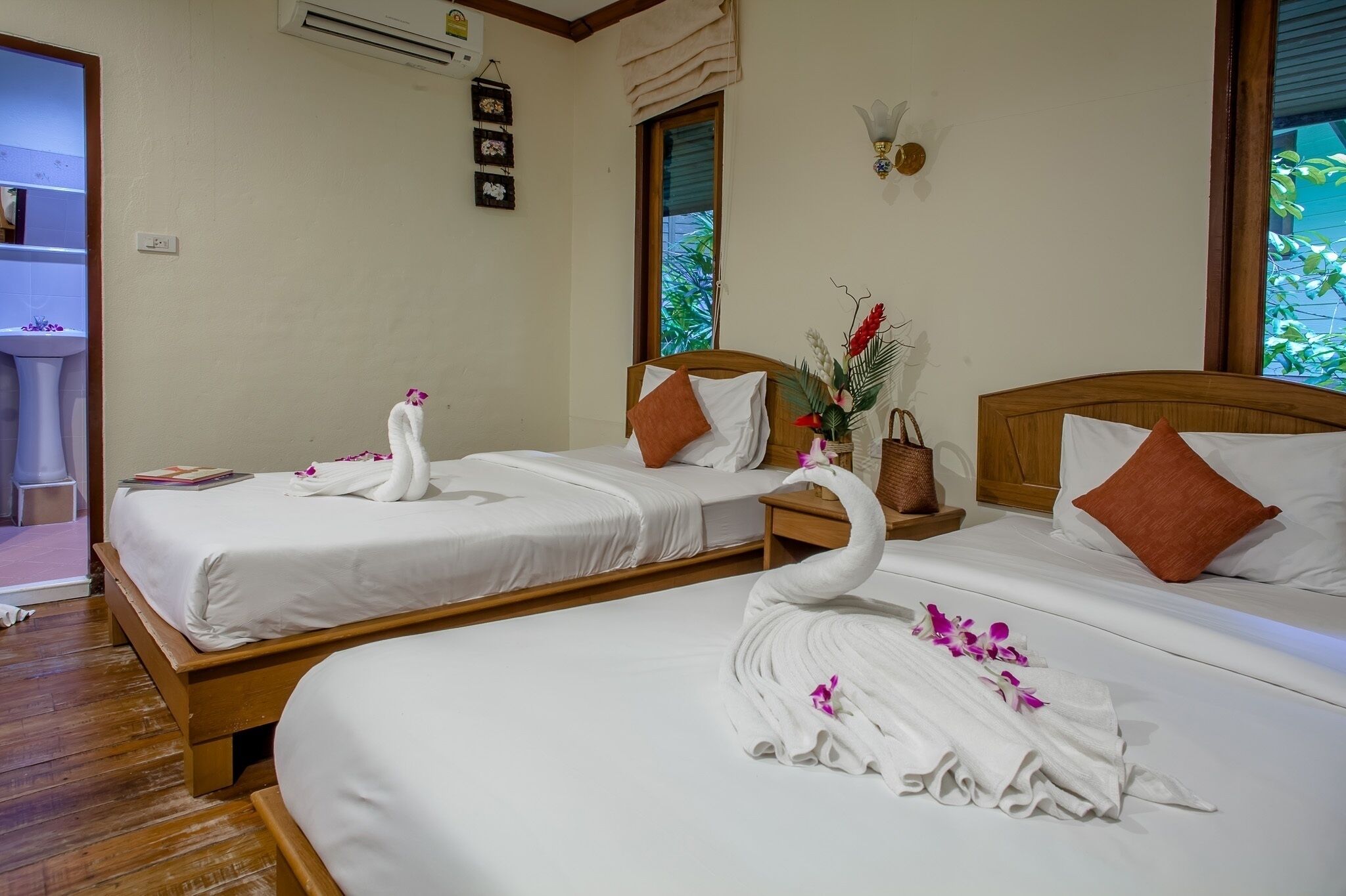 Habitación de hotel con dos camas, cabeceros de madera, ropa de cama blanca y toallas dispuestas en forma de cisnes con flores.