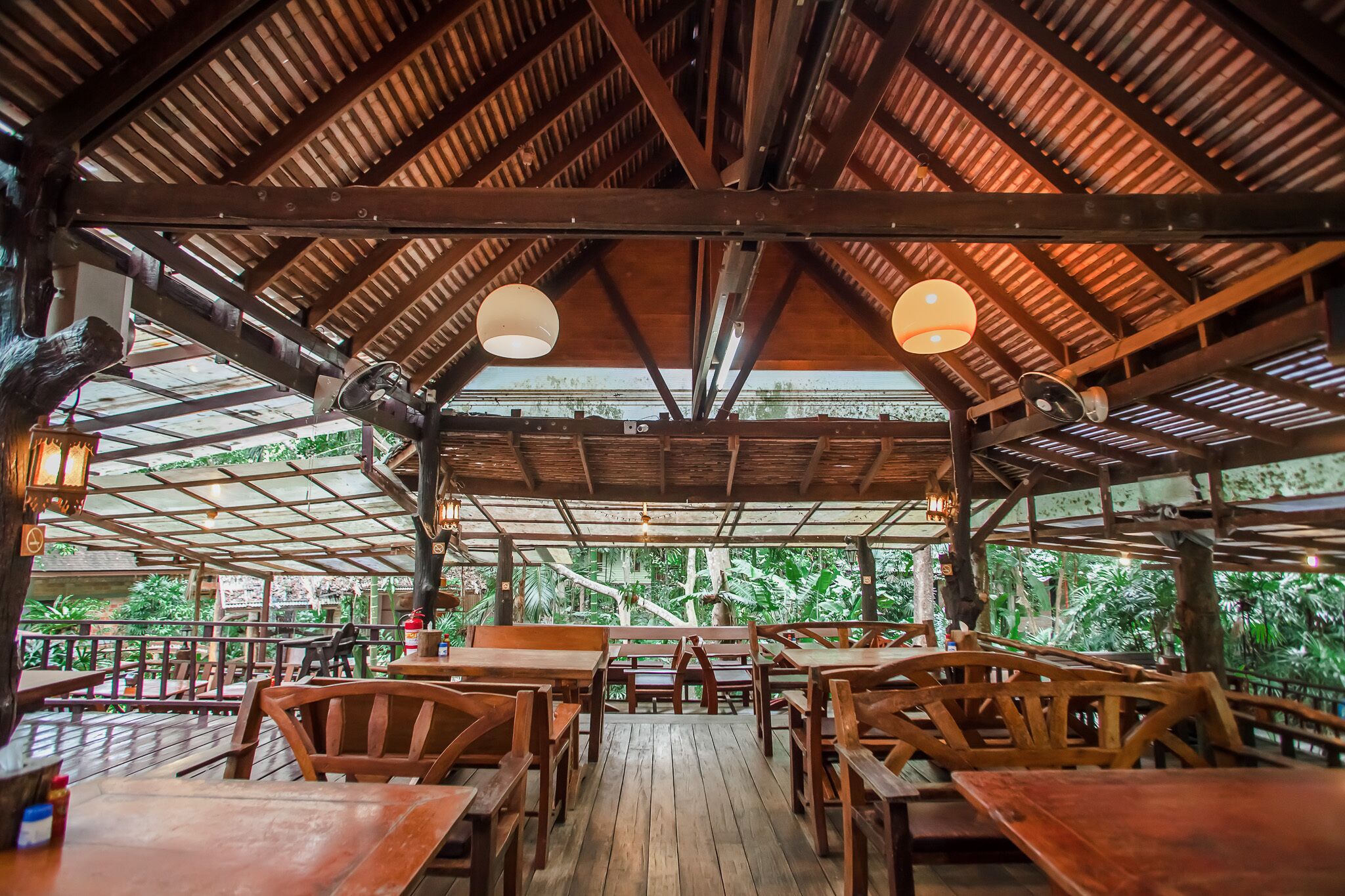 An outdoor wooden deck with tables and chairs, surrounded by lush greenery.