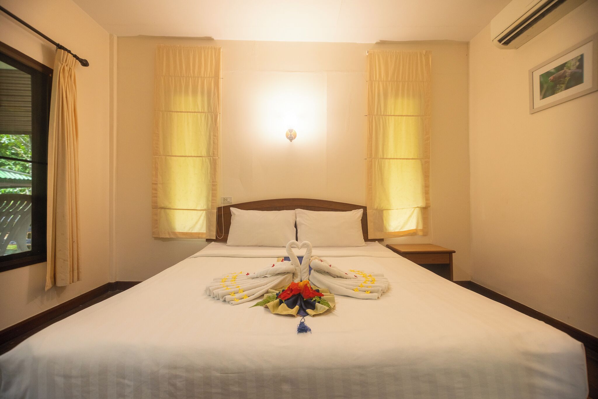 Habitación de hotel con una cama bien hecha, dos mesitas de noche, una lámpara de pared y cortinas en las ventanas.