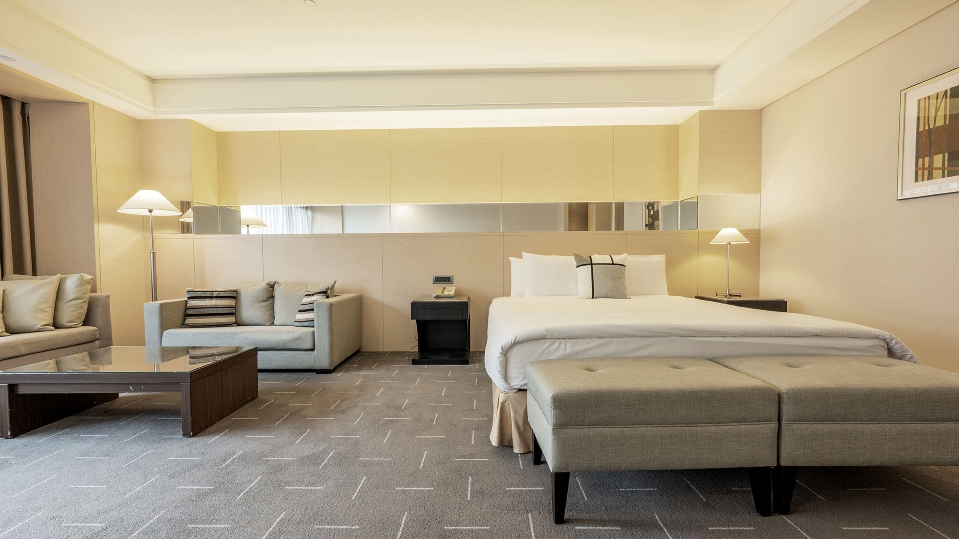 Una habitación de hotel moderna con una cama, un sofá, una mesita de café y una mesita de noche con lámpara.