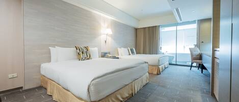 A hotel room with two beds, a desk, a chair, and a large window.