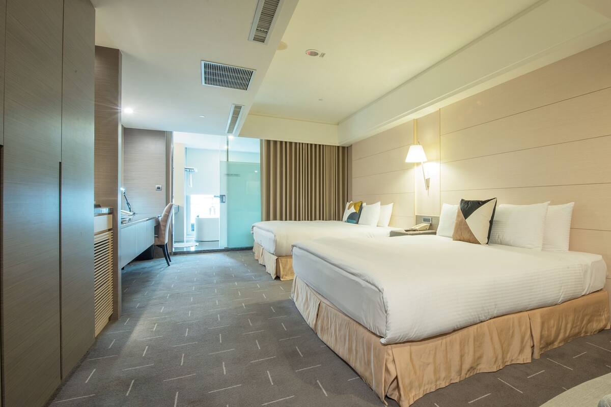 A hotel room with two beds, a desk, and a bathroom visible through an open door.