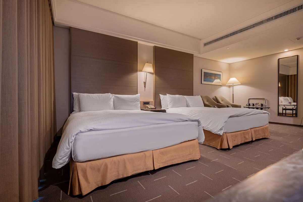 A hotel room with two beds, a desk, a chair, a mirror, and a lamp.
