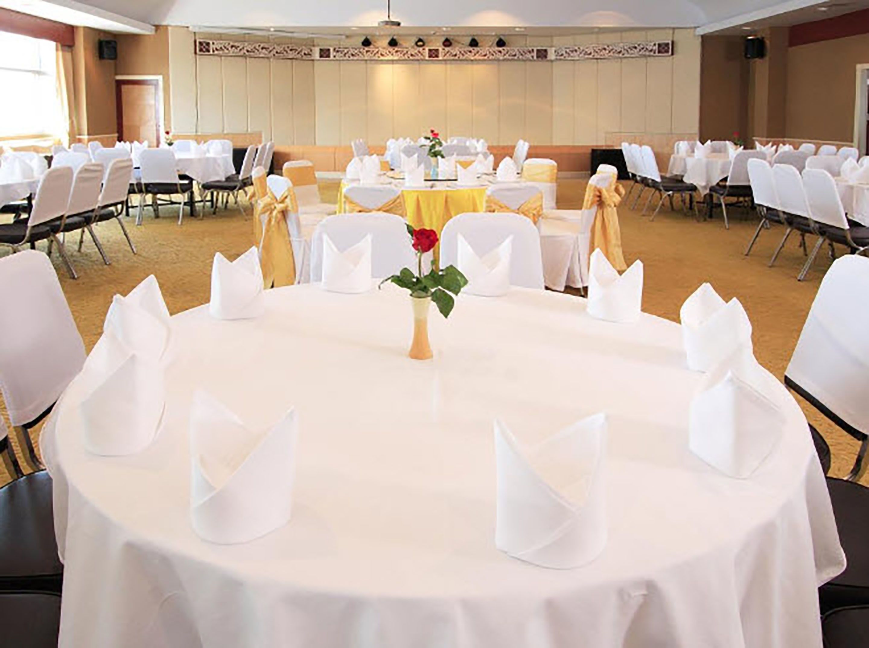 Een feestzaal met ronde tafels, ingericht voor evenementen, met witte tafelkleden en stoelen met gouden linten.