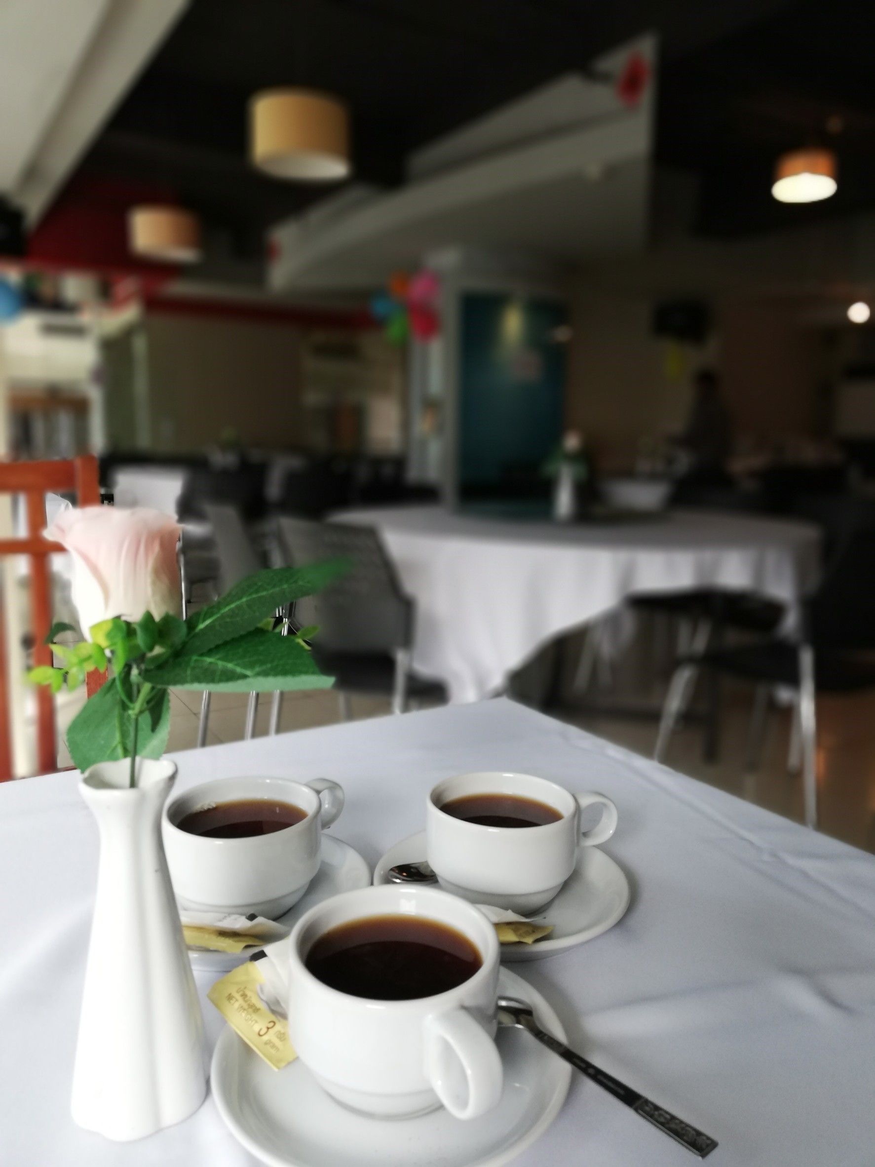 Une table avec trois tasses à café blanches, un vase blanc contenant une seule rose et un petit pichet blanc.