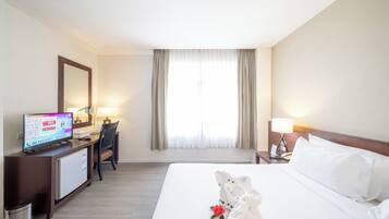 Habitación de hotel con cama, escritorio con computadora, una silla y ventana con cortinas.