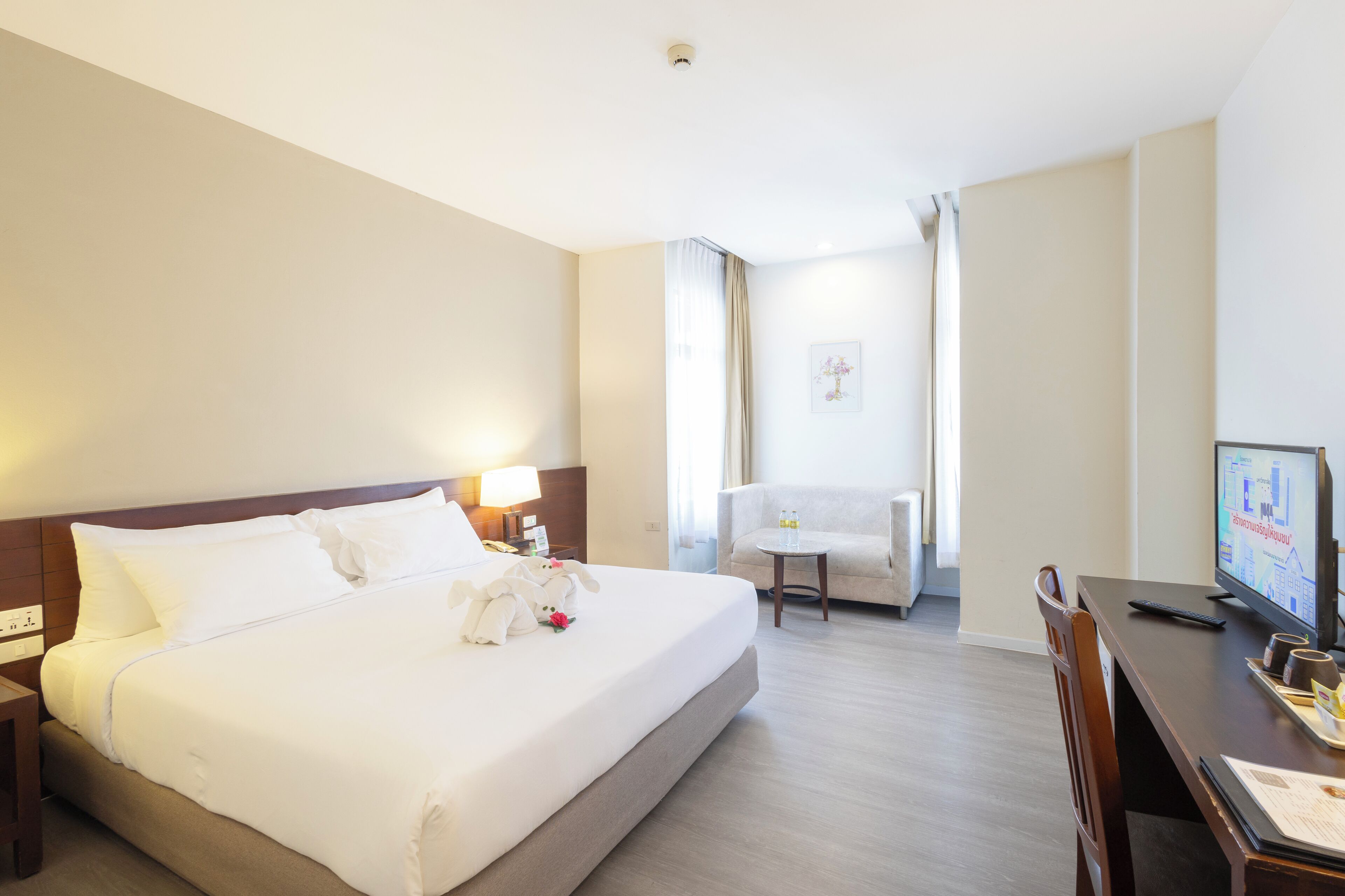 A hotel room with a large bed, a desk with a computer, a chair, and a small table.