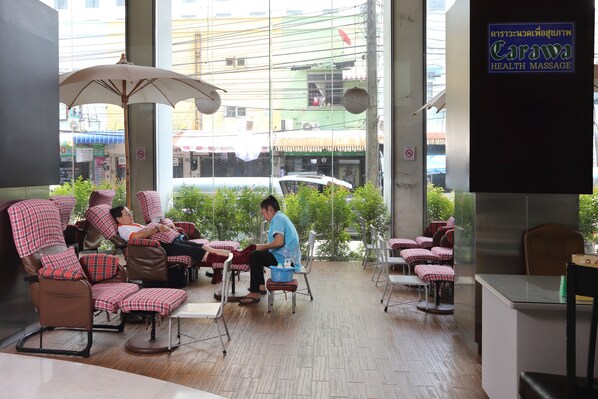 Un salón de masajes con varias sillas de masaje, un mostrador de recepción y un amplio ventanal con vistas a la calle.