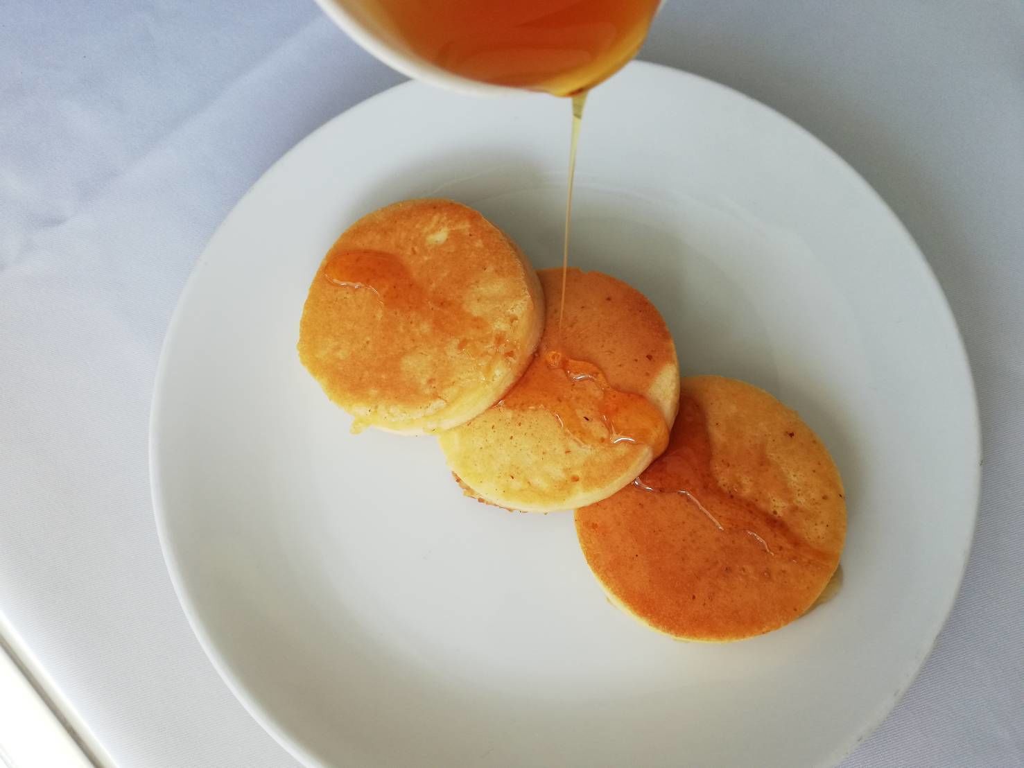 A plate with three pancakes and syrup being poured over them.