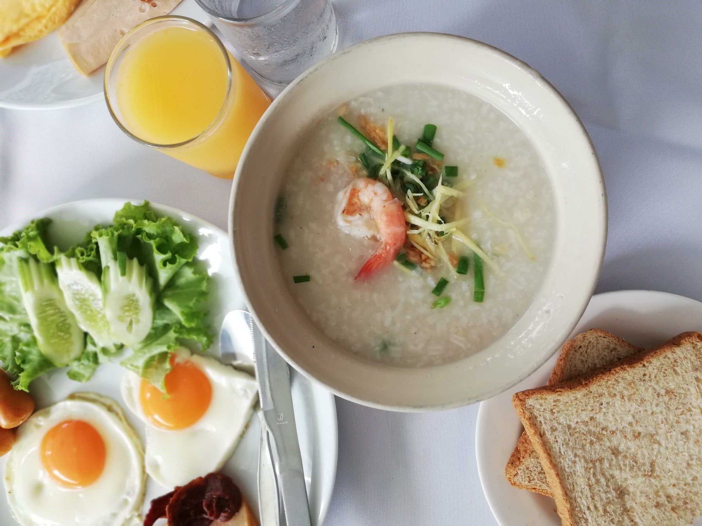 A breakfast plate with eggs, toast, soup, and a glass of orange juice.