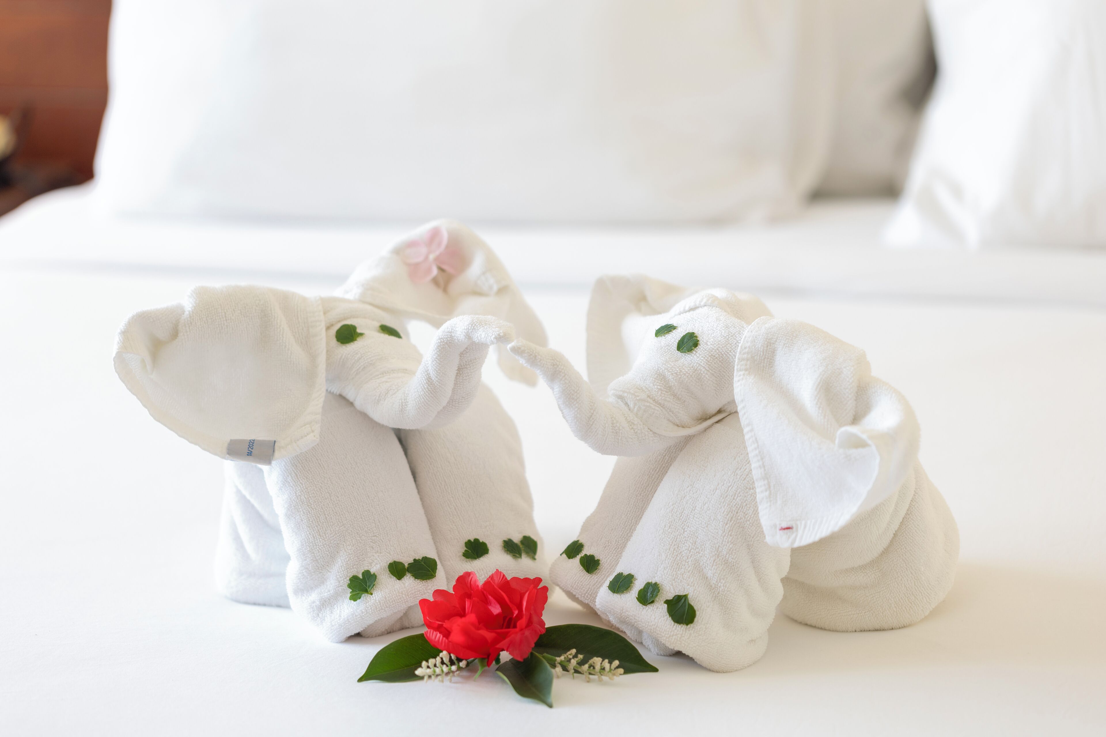 Two plush elephant-shaped towels with green leaf patterns and a red flower on a white surface.