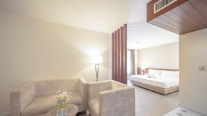 A hotel room with a sofa, a small round table with a vase of flowers, a bed, and a large window. - Golden Crown Grand Hotel (Hat Yai)