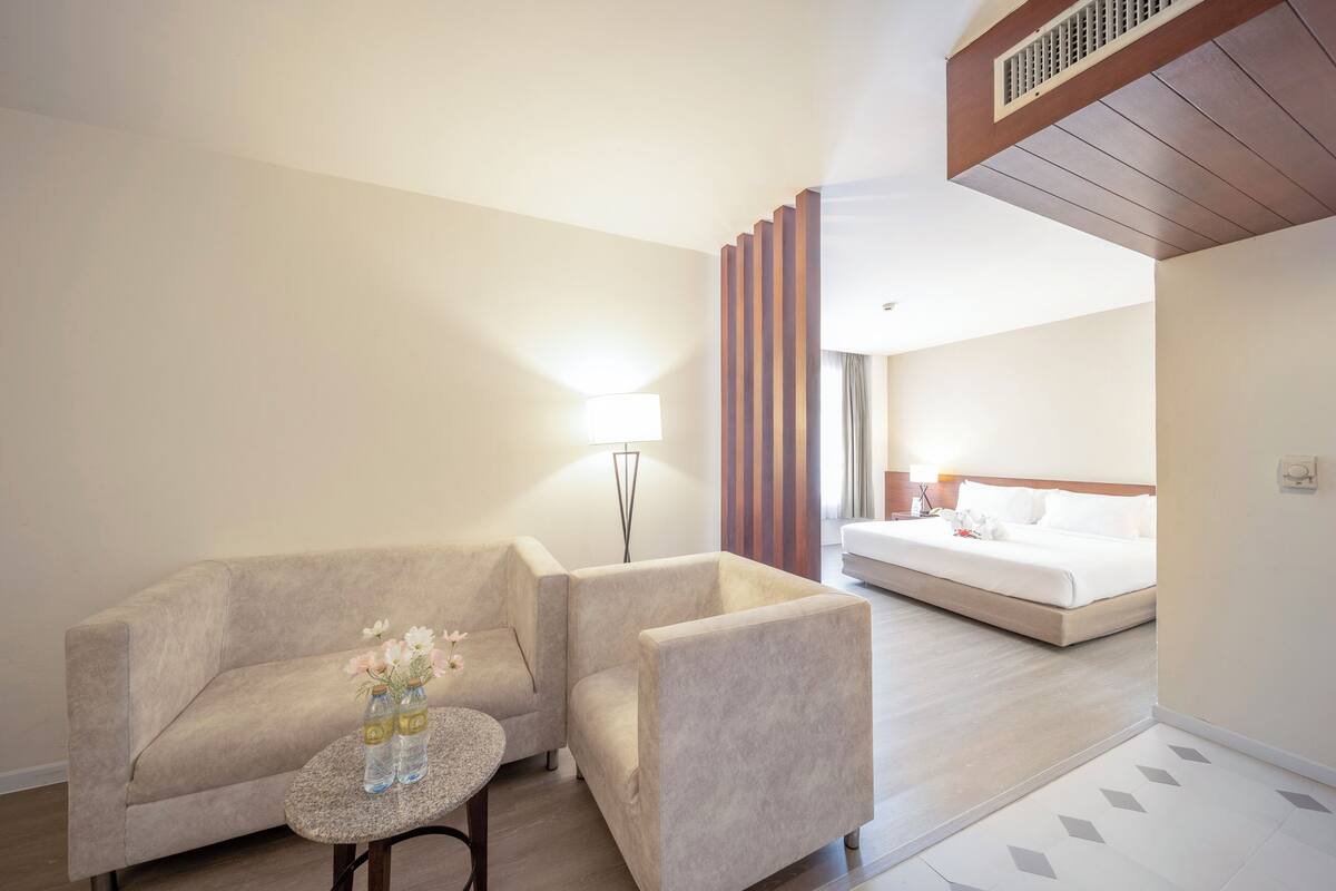 A hotel room with a sofa, a small round table with a vase of flowers, a bed, and a large window.