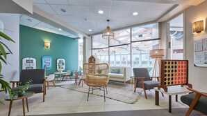 A modern waiting area with a green accent wall, wicker chairs, and a large window providing natural light. - Residence Pierre & Vacances Le Chant des Oiseaux (Courseulles-sur-Mer)