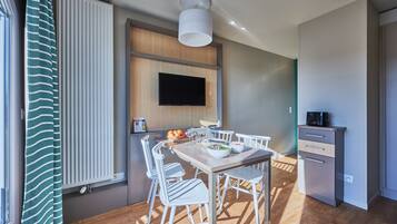 A modern kitchen with a wooden table, white chairs, a built-in oven, and a flat-screen TV mounted on the wall.