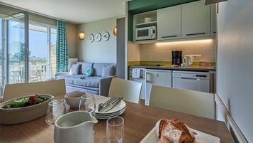 A dining area with a table set for two, a microwave, and a coffee maker in the kitchen.