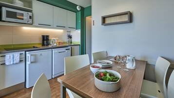 A modern kitchen with white cabinets, a microwave, a coffee maker, and a dining table set with plates, glasses, and a bowl of salad.