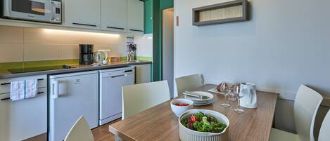 A modern kitchen with white cabinets, a microwave, a coffee maker, and a dining table set with plates, glasses, and a bowl of salad.