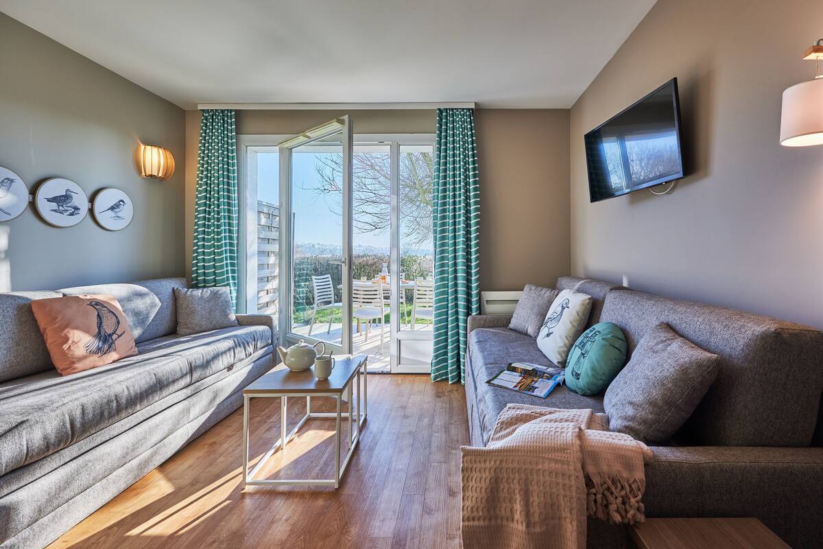 A modern living room with two sofas, a coffee table, and a flat-screen TV mounted on the wall.