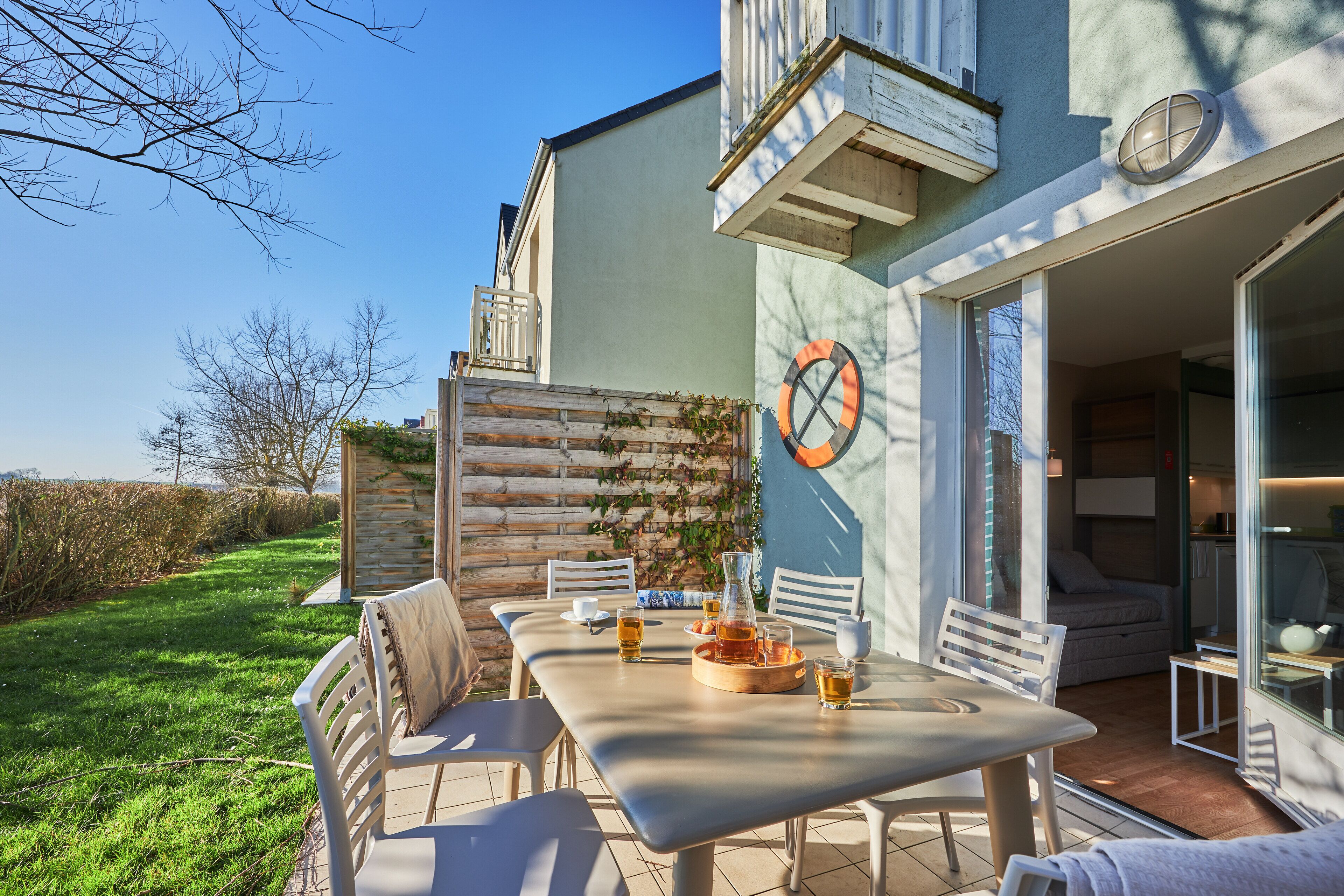 An outdoor patio with a table set for dining, surrounded by chairs, and a wooden fence with climbing plants.
