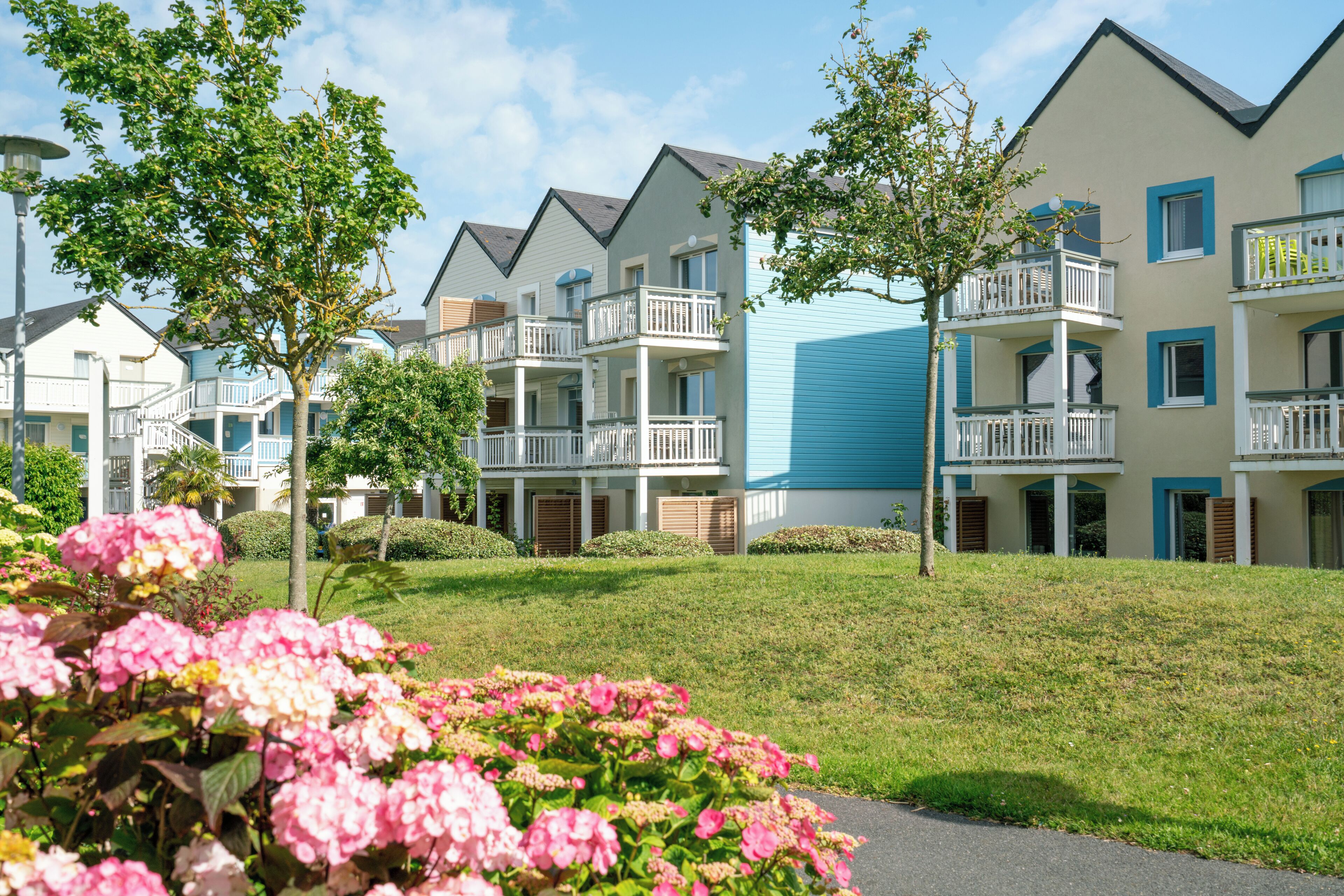 A residential building with multiple balconies, a well-maintained lawn, and a clear sky.