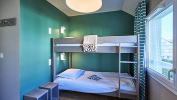 A bunk bed room with a window, a bedside table, and a lamp.